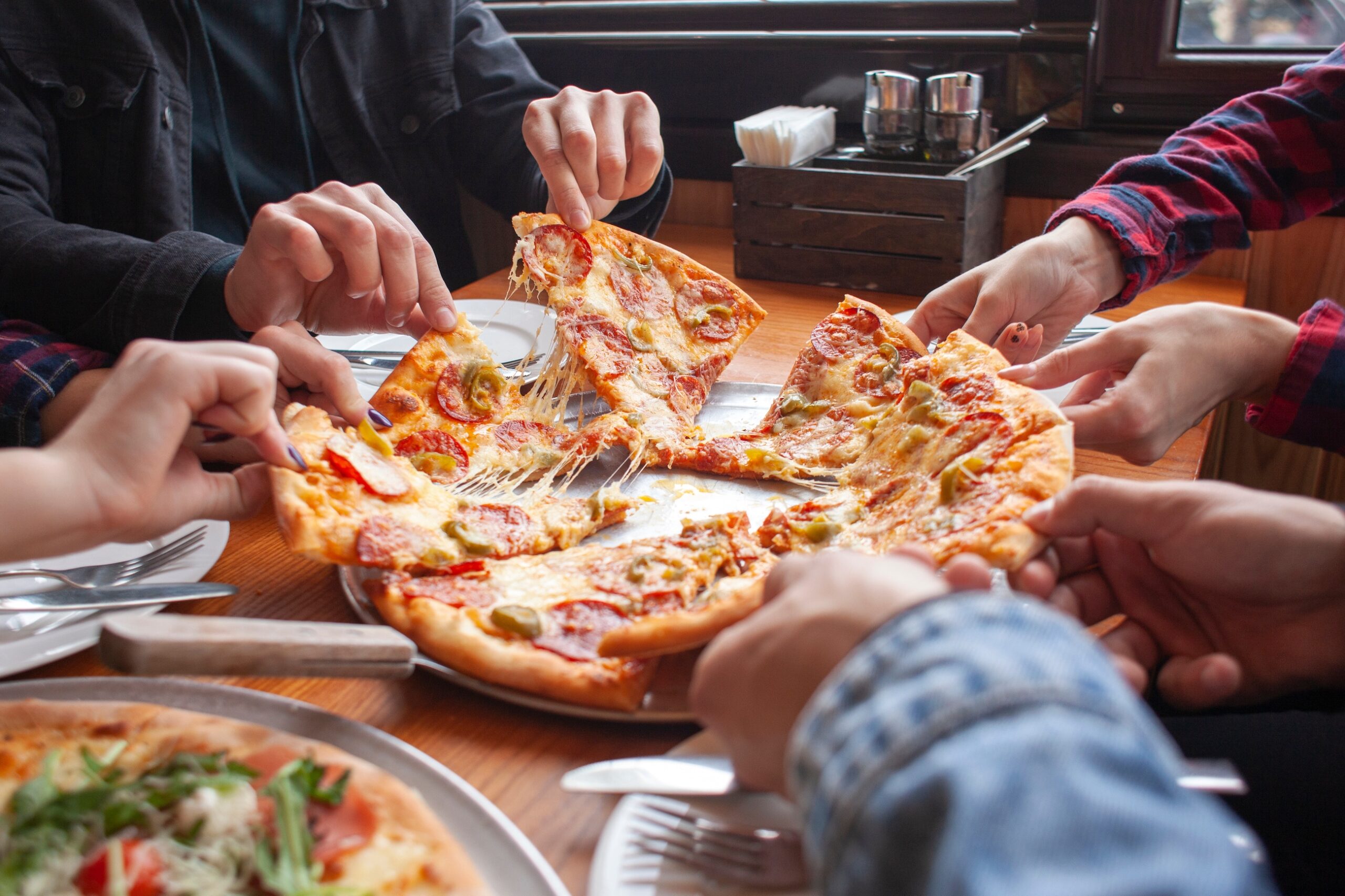 group of students friends eat Italian pizza, hands take slices of pizza in a restaurant