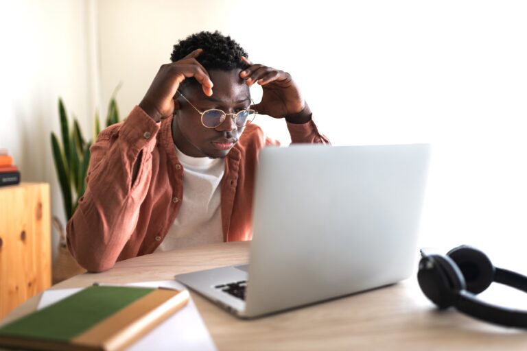 African American black male college student stressed and overwhelmed studying in front of laptop.